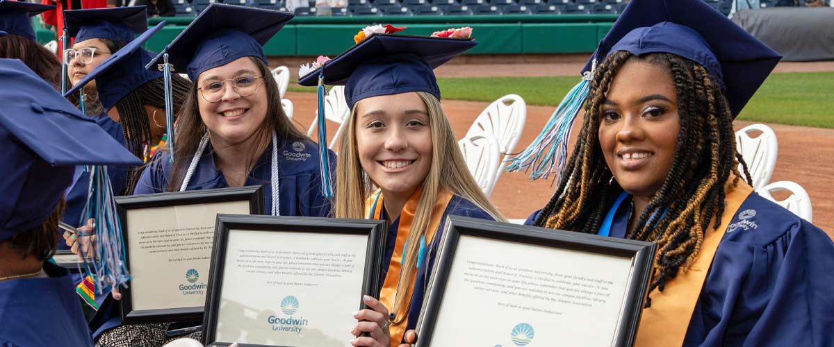 three graduates sitting, smiling, and holding up diplomas