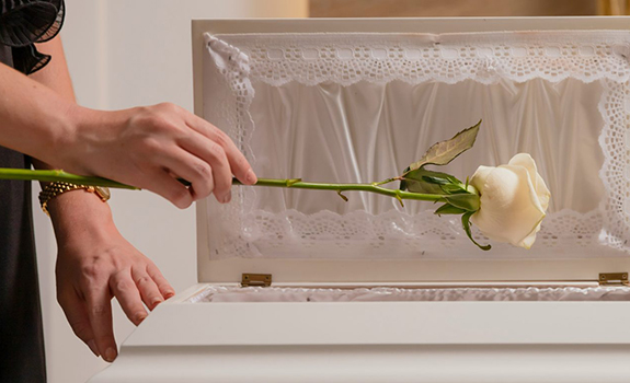 hand holding a white rose over a casket